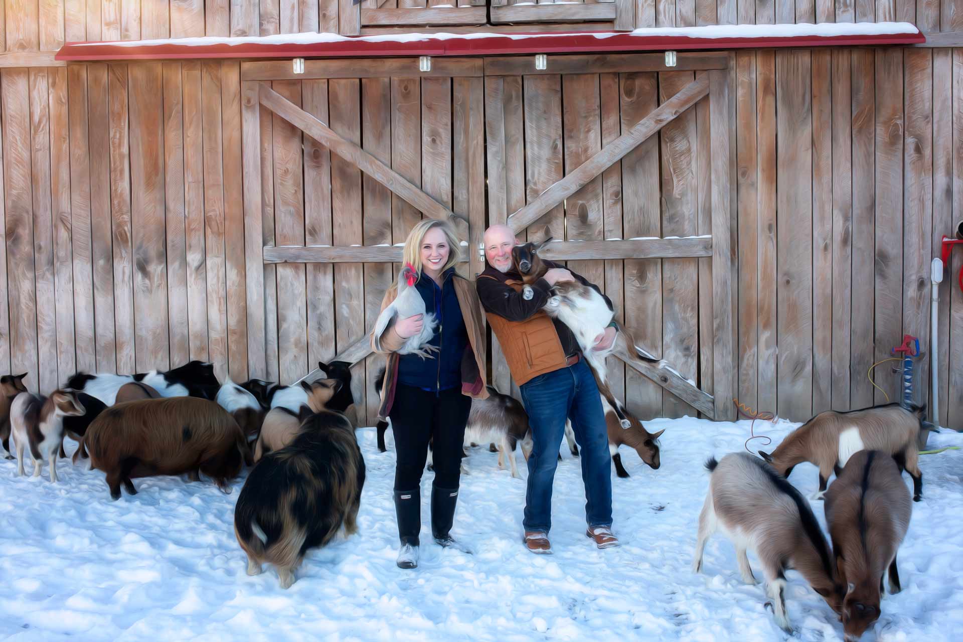 Couples standing in front of their barn in the snow surrounded by their farm animals during professional photography session at Moments By T Franklin Tennessee