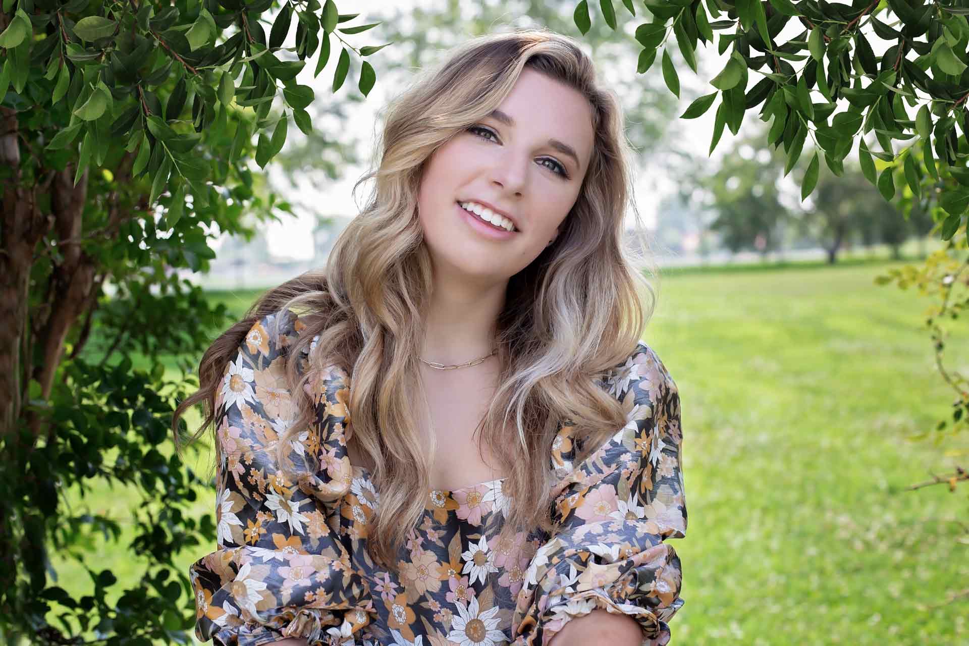 Blonde high school senior with wavy hair sitting in the grass during a professional senior photography session at Moments By T, Franklin Tennessee