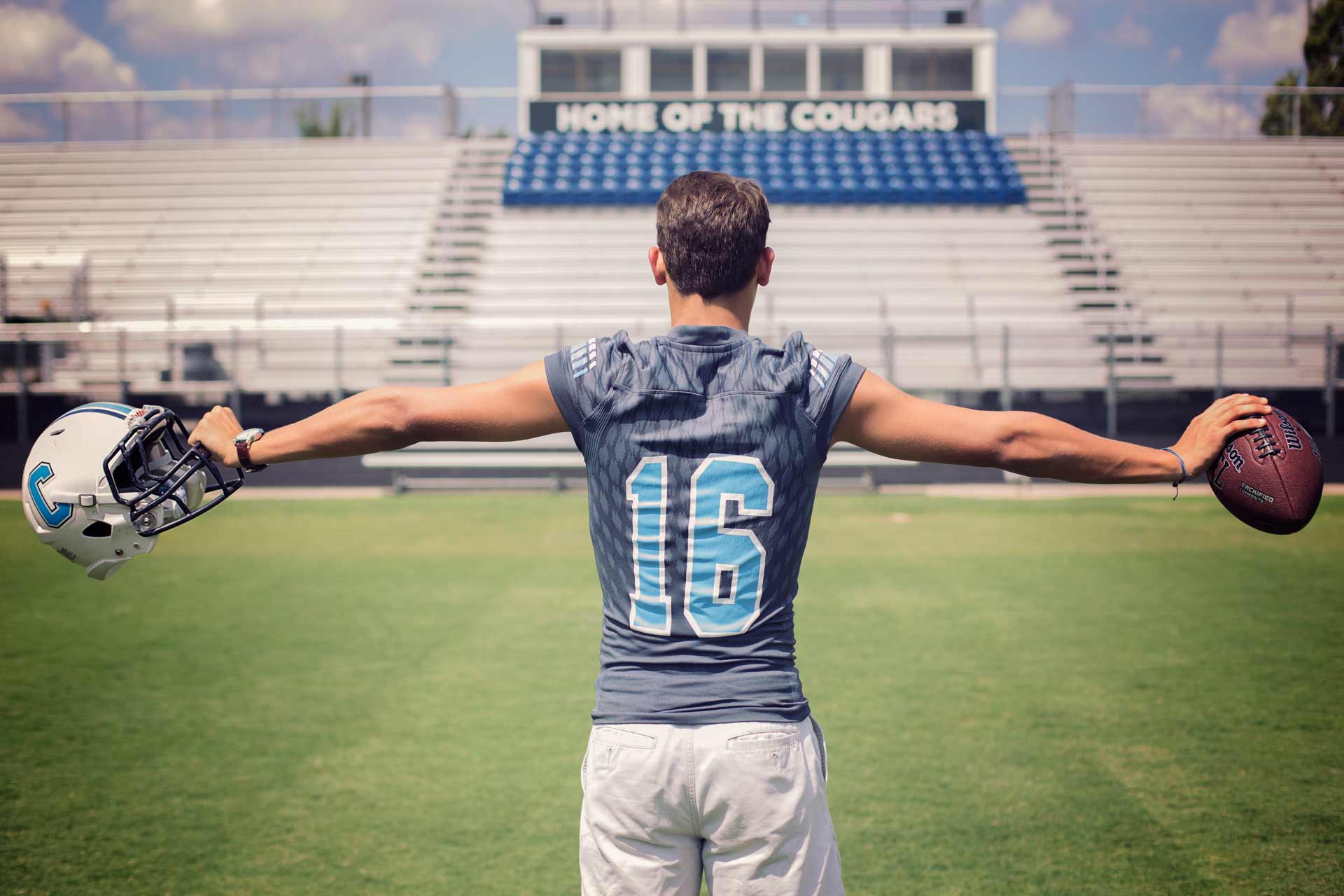 High school senior boy wearing his football gear and holding his helmet and ball in his hands during a professional senior photography session at Moments By T, Franklin Tennessee