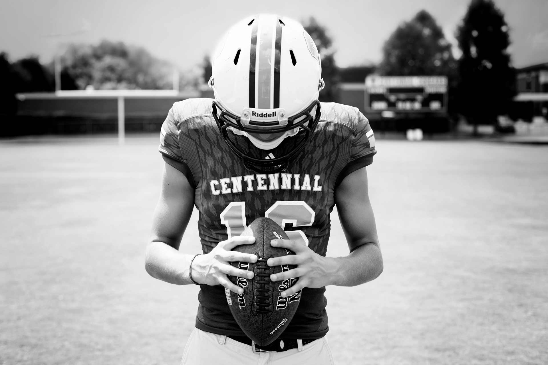 High school senior boy wearing his football gear and holding his ball in his hands during a professional senior photography session at Moments By T, Franklin Tennessee