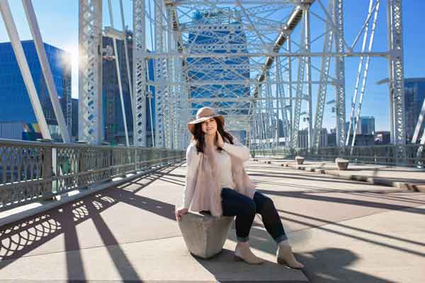 A teenage woman wearing a skinny jeans, pink furry vest and a floppy hat on the pedestrian bridge in downtown nashville. photoshoot at Moments By T in Franklin TN 