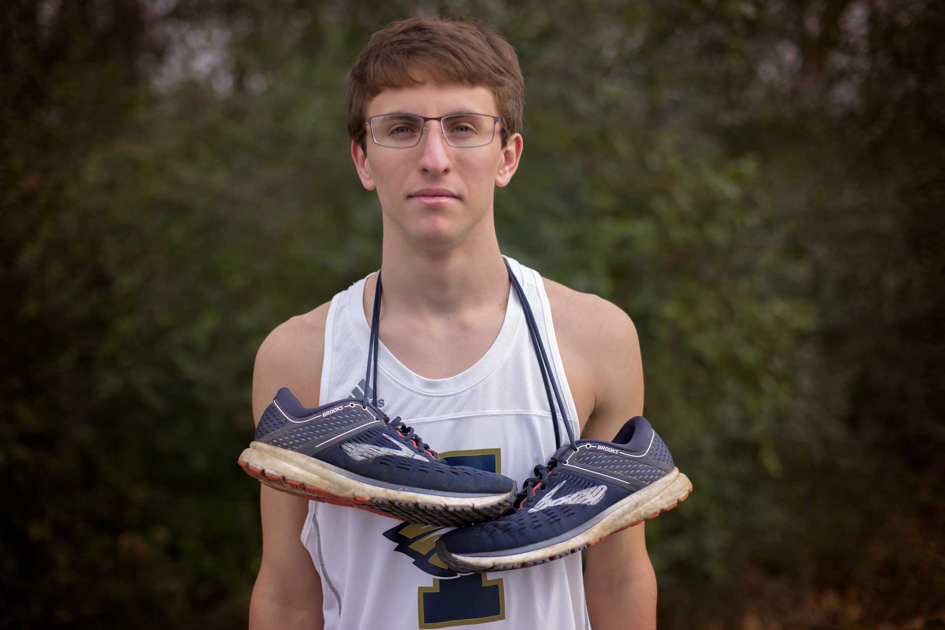 High school senior boy standing in a tank with his running shoes around his shoulders during a professional senior photography session at Moments By T, Franklin Tennessee