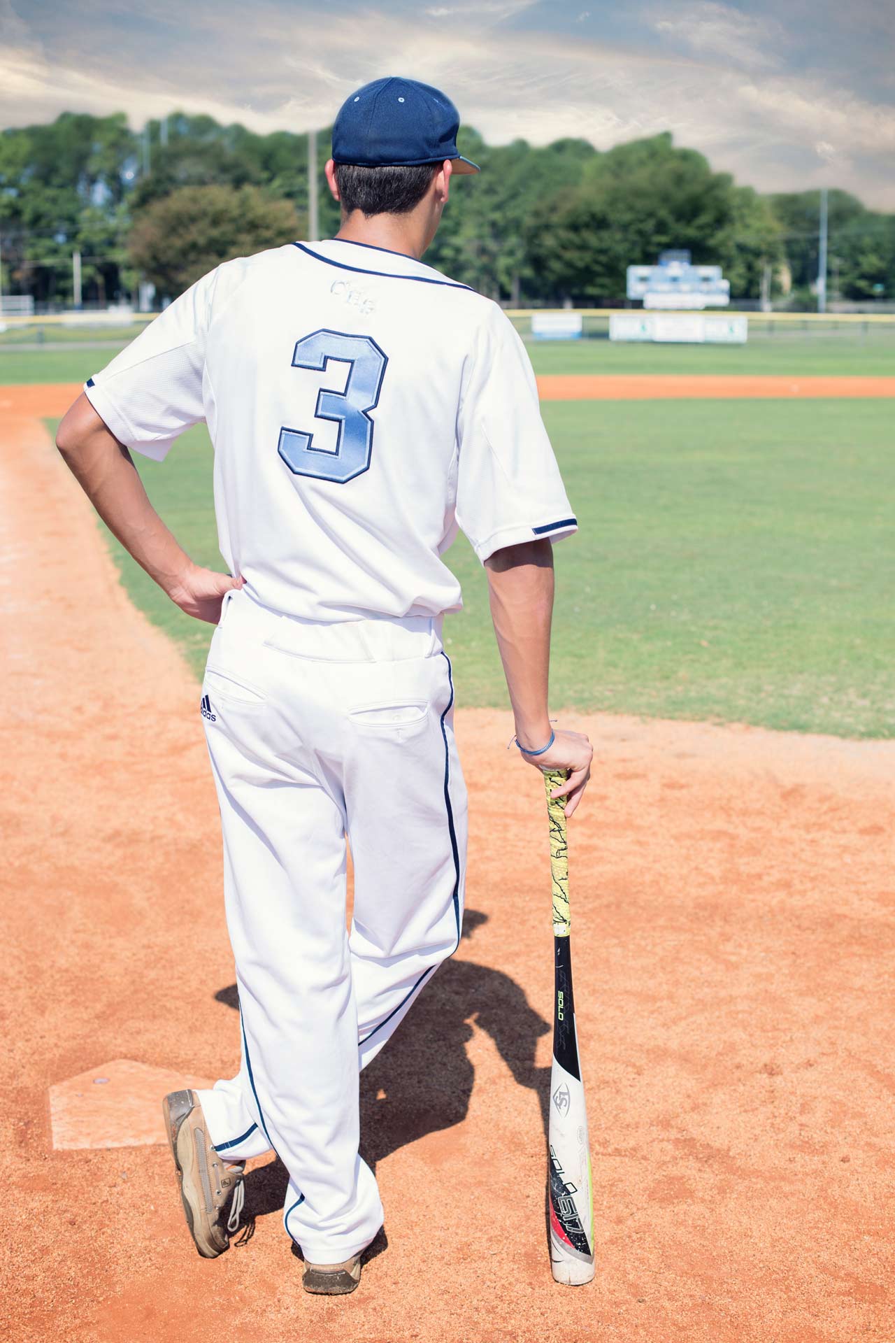 Baseball player standing with his back to the camera leaning on a bat during a professional senior photography session at Moments By T, Franklin Tennessee