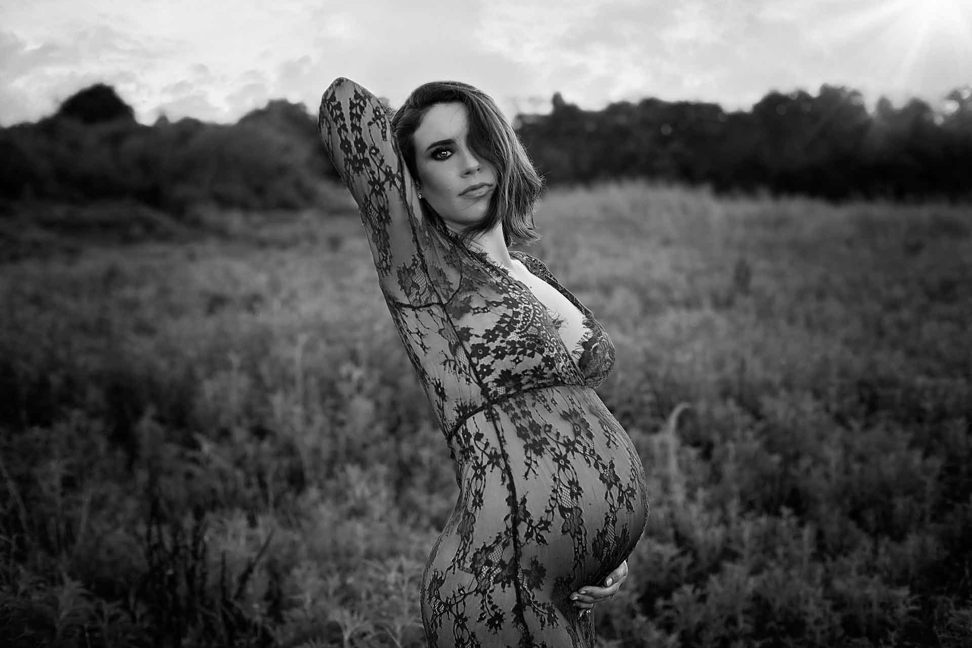 a woman standing in an open field wearing a see through robe showing off her pregnancy belly